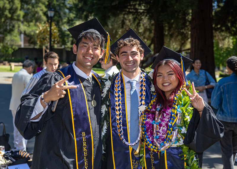 Three graduates smile and make peace signs at the camera