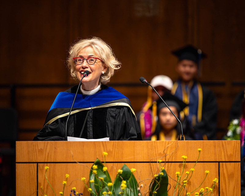 Faculty with red glasses speaks at podium during commencement