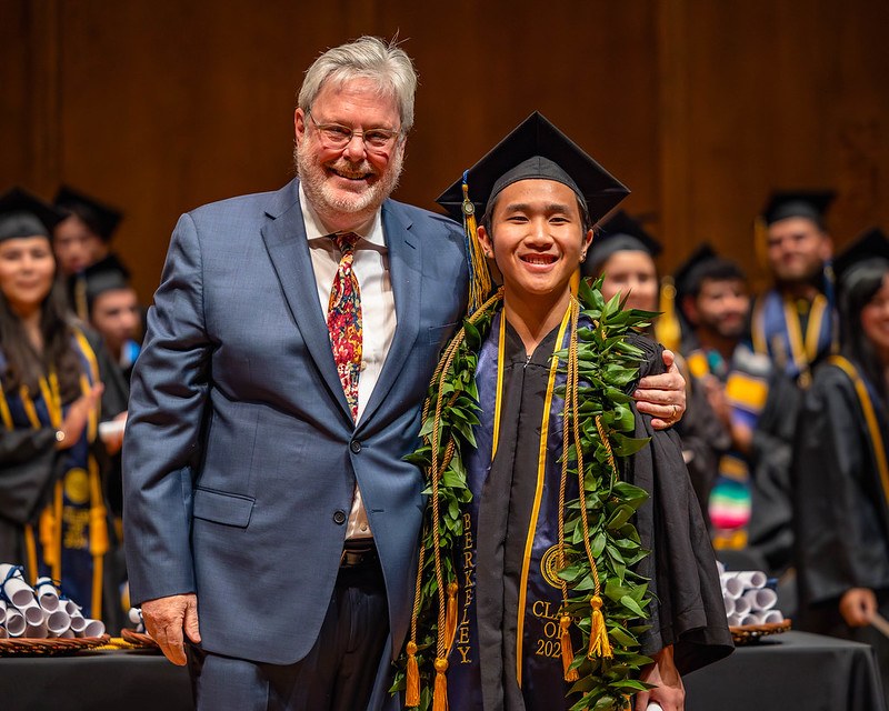 Faculty member stands with arm around graduate student smiling