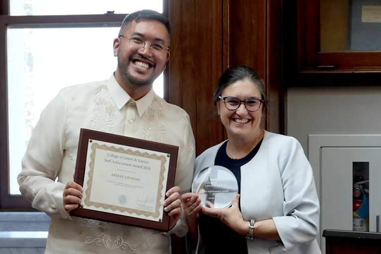 A man and a woman stand together, holding awards