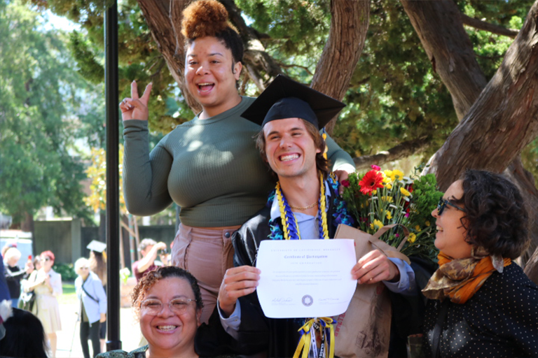 Graduate holds his diploma and poses with loved ones