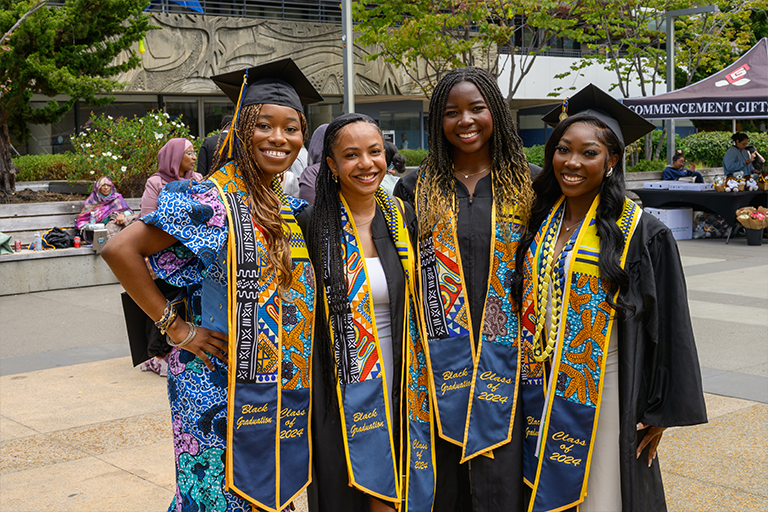 Four graduates in regalia smile at camera