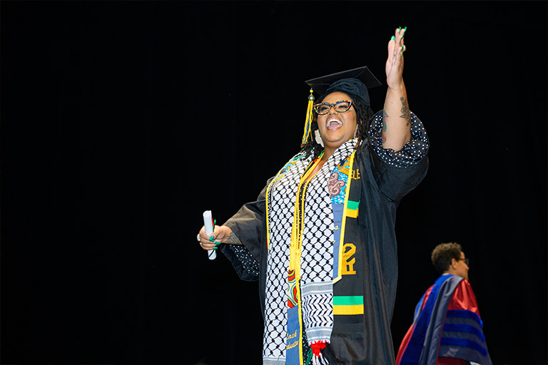 Graduate with her hand up and smiling during commencement