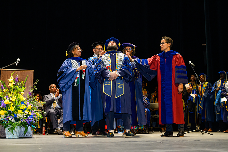 Graduate student receives support from faculty upon being hooded at commencement
