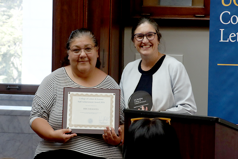 Two women hold awards and pose together