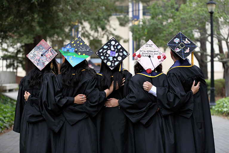 Five graduates from behind, arms linked and caps decorated
