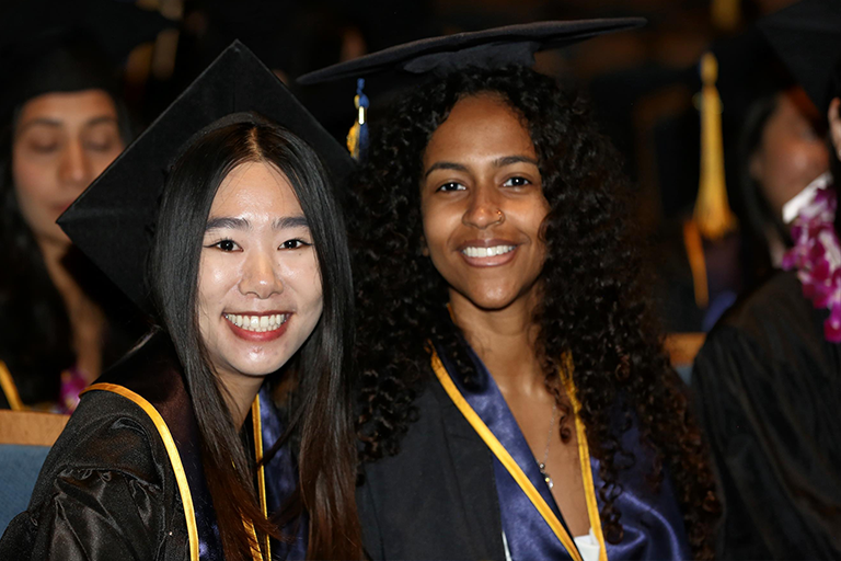 Two graduates smile at the camera