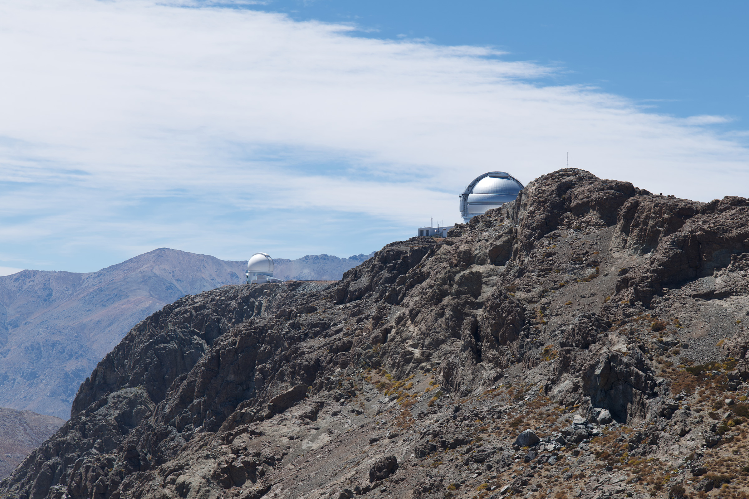 Buildings at the Cerro Tololo Inter-American Observatory peer over a rocky outcropping.