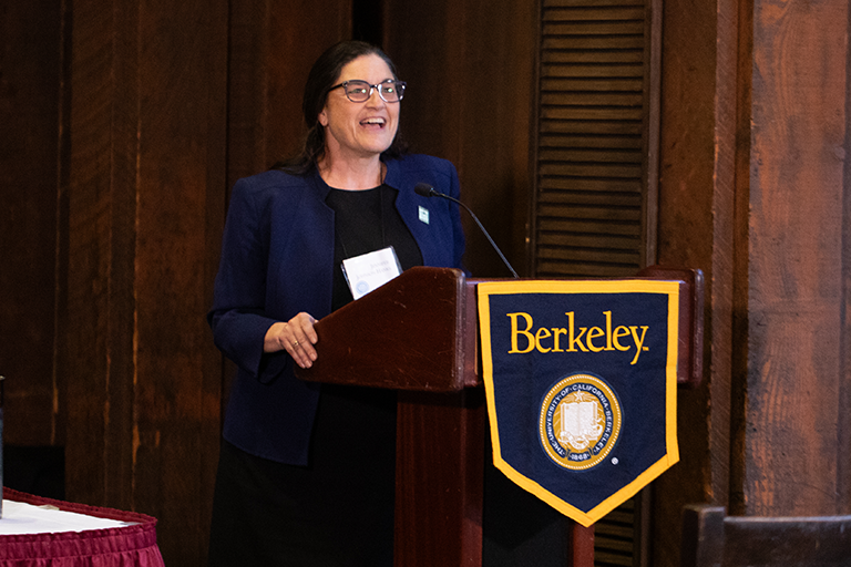 Woman speaks at a podium. Podium has a Berkeley banner displayed on it.