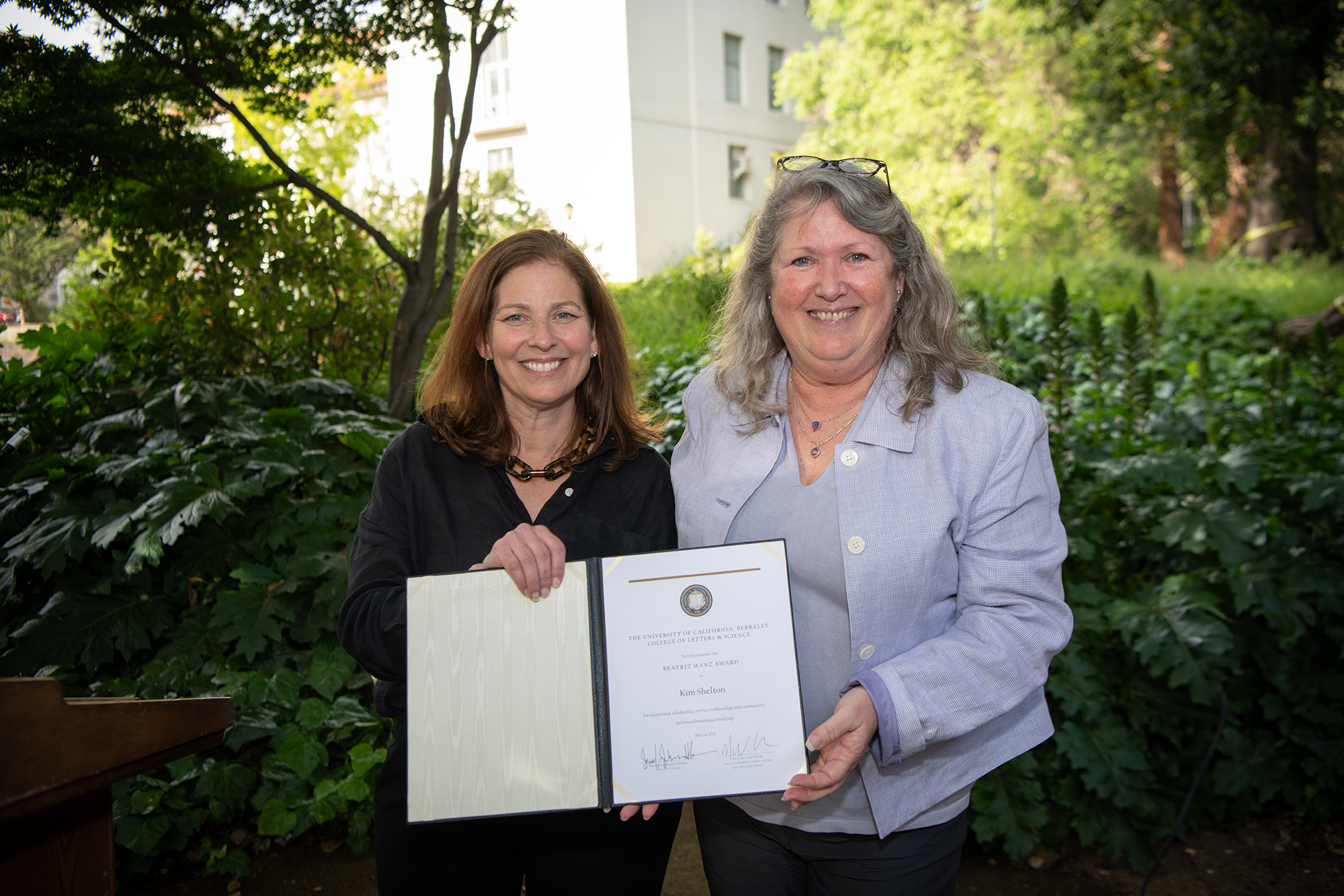 Two people stand outside, holding up an award certificate