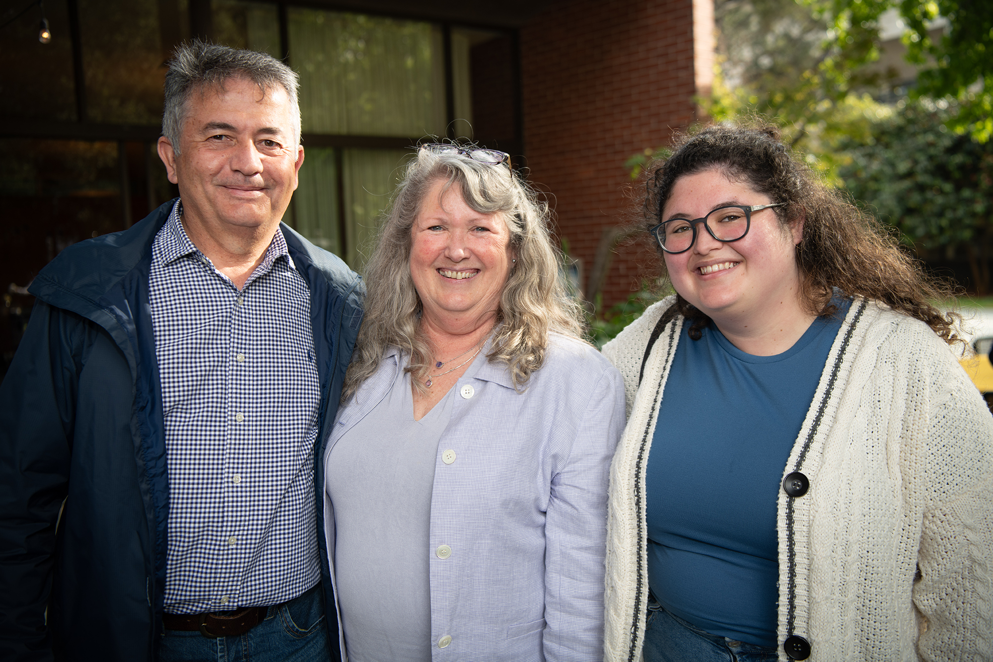 Three people standing close together, smiling at camera