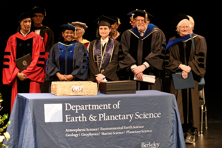 Faculty in regalia stand in front of a table with Earth & Planetary Science branding