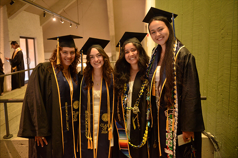 Four graduates in regalia smile at camera