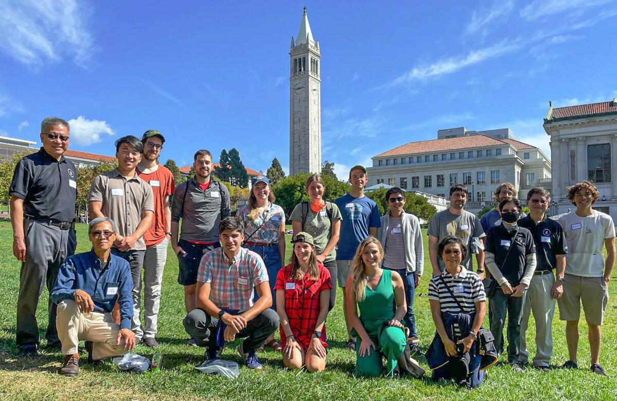 Eighteen people stand and kneel for a group photo in front of the Campanile on Berkeley's campus.