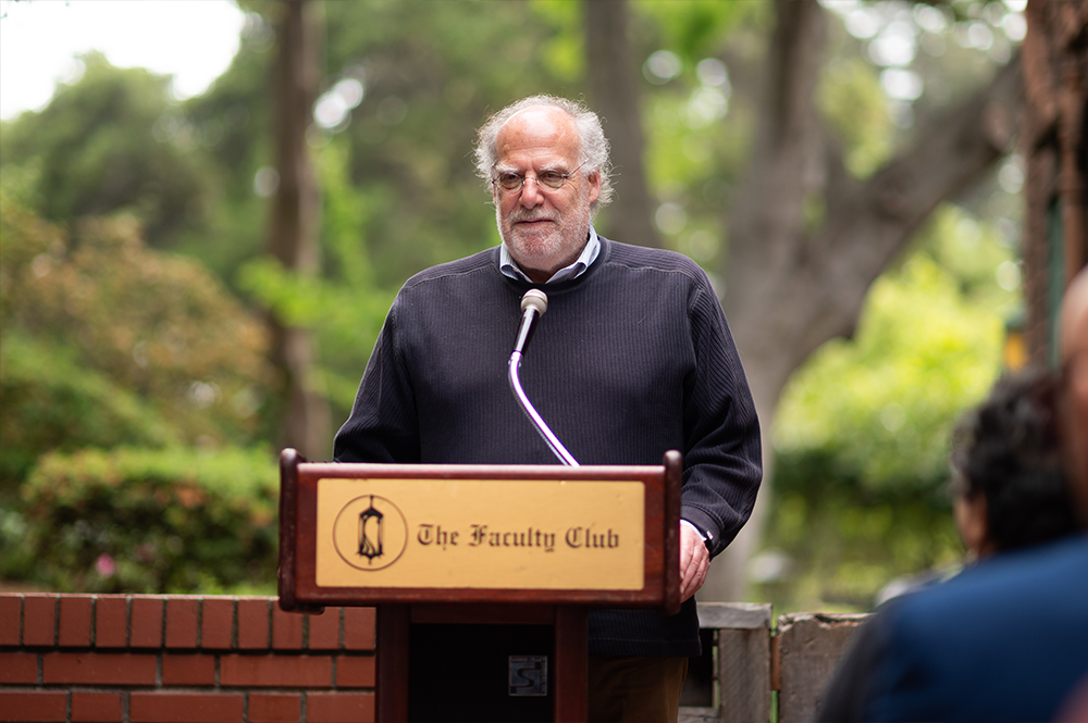 Dean Steven Kahn, man wearing dark sweater over a collared shirt, speaks at podium