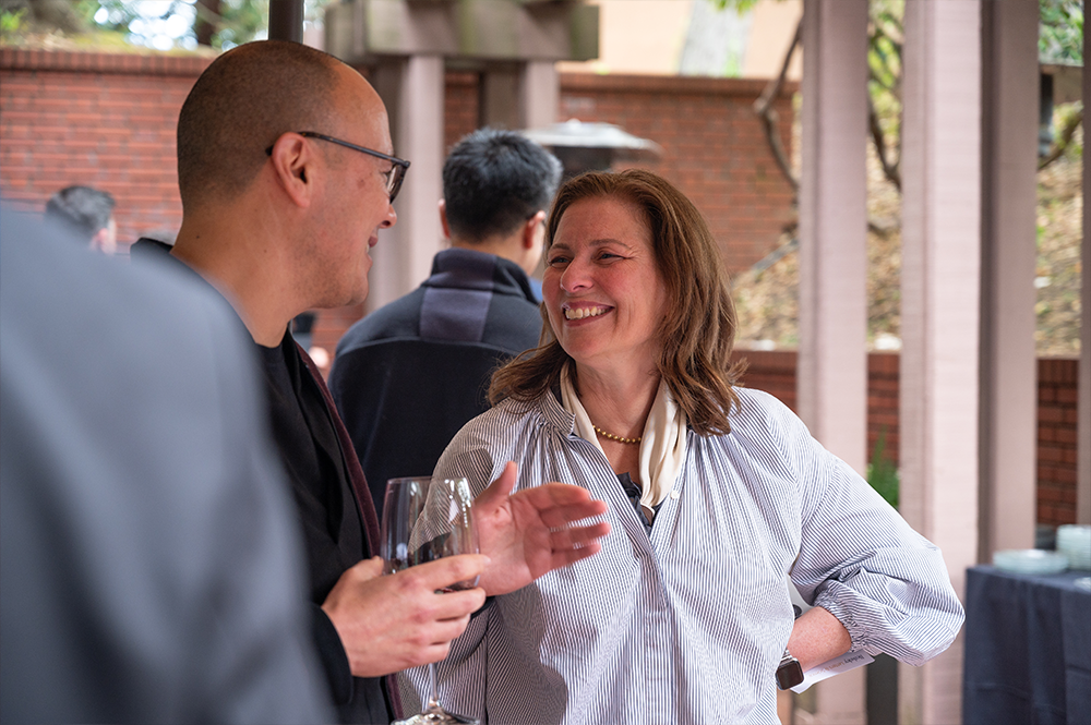 Woman with shoulder length brown hair smiles up at a man holding a wine glass outdoors