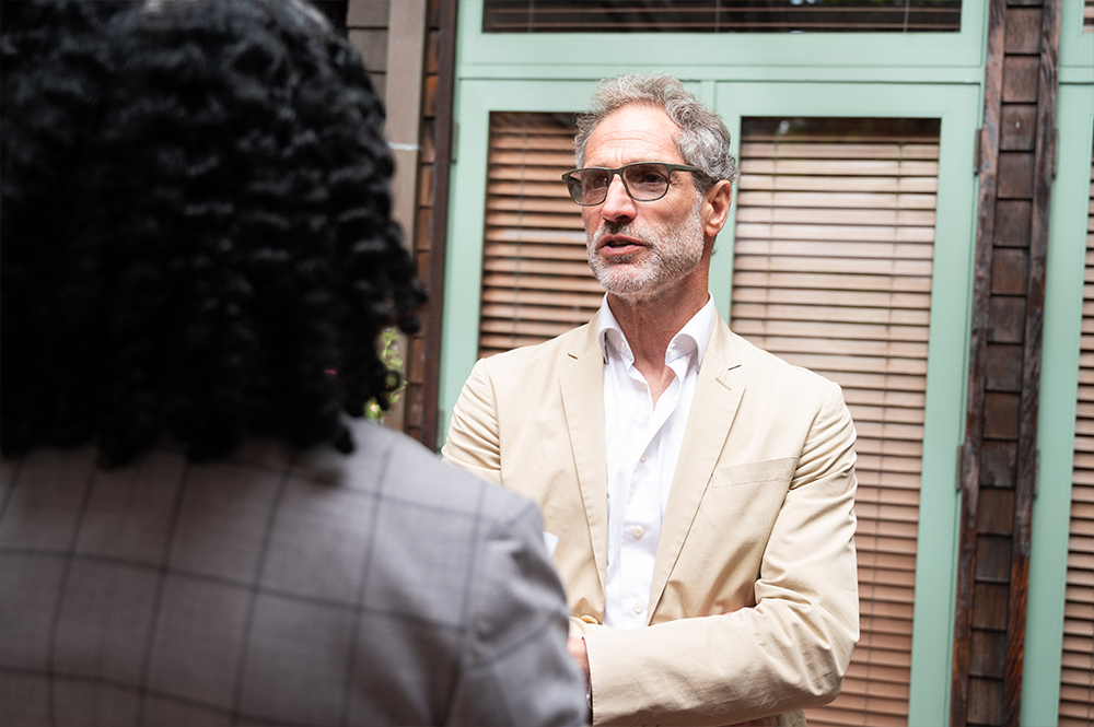 Man with short hair and beard in a white collared shirt and tan sports coat in conversation