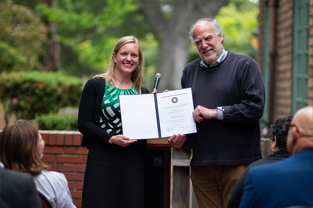 Two people accepting an award together, holding up a certificate