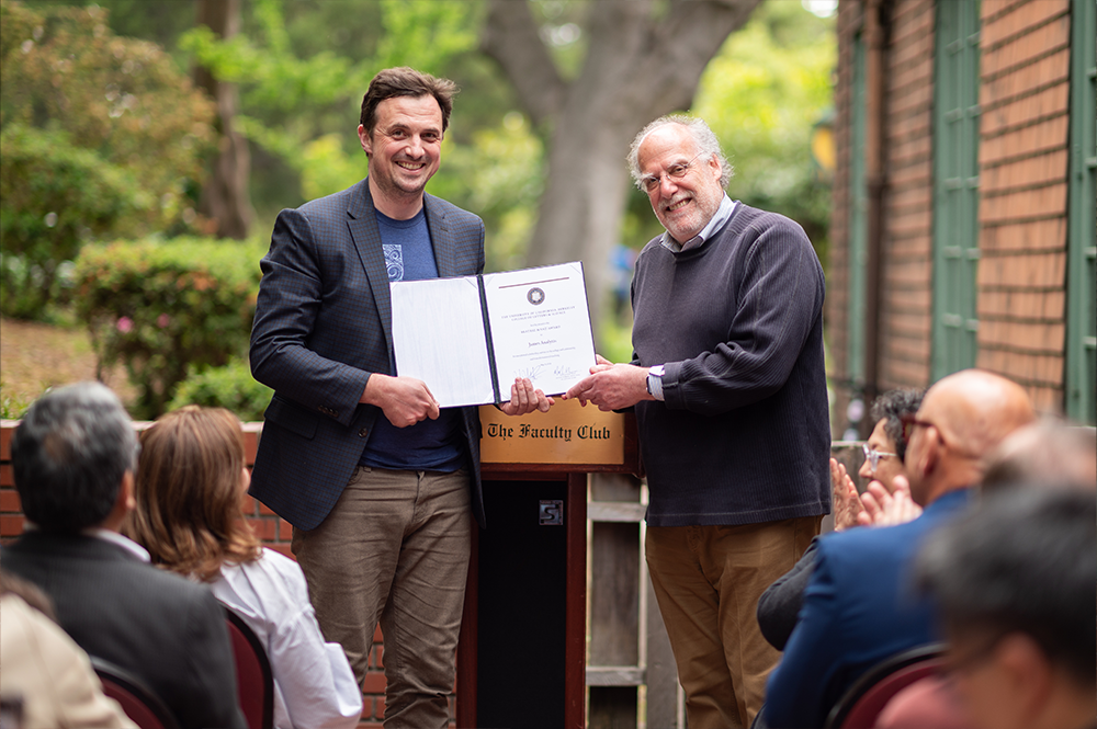 Two men hold an award together in front of a podium