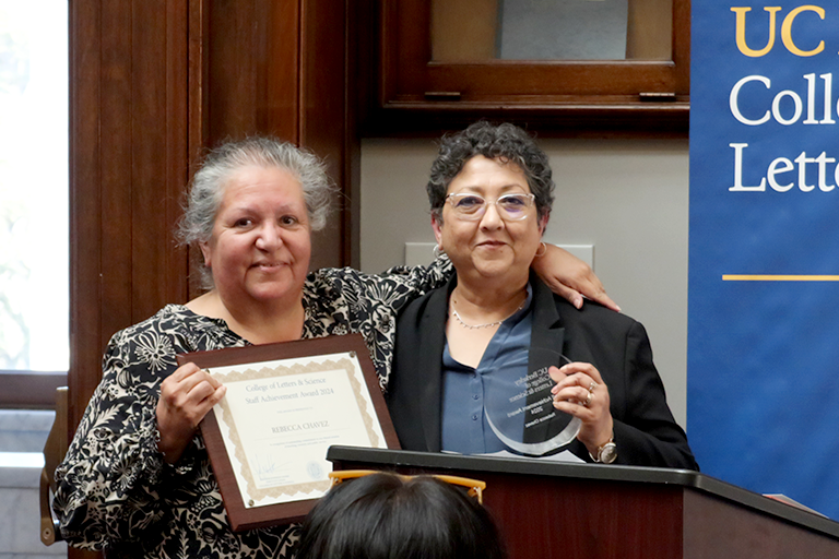 Two woman hold awards and pose together