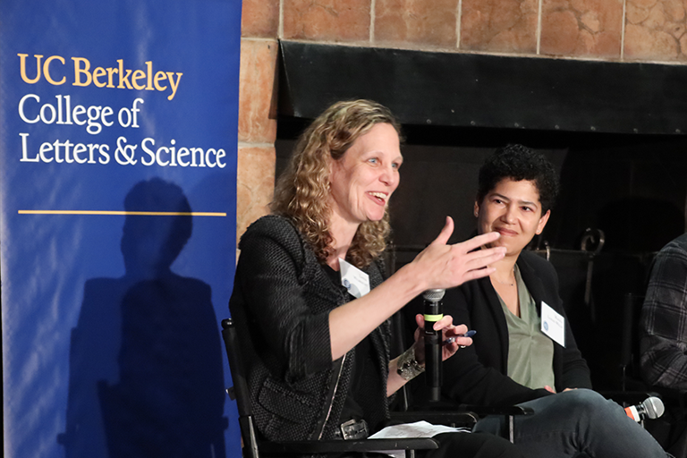 Woman panelist speaks into a handheld mic as another panelist smiles and looks at her