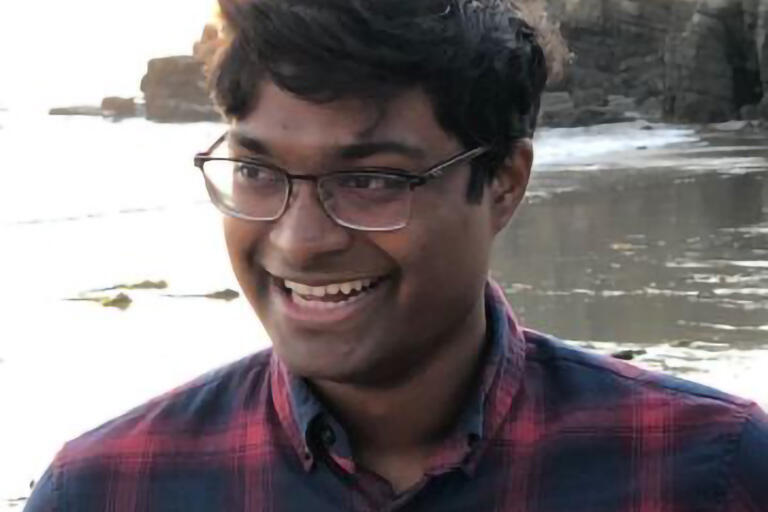A man wearing a red, plaid shirt smiles on a beach