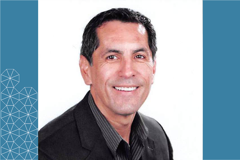 Headshot of Sergio Garcia, man with dark hair wearing dark blazer and striped button up