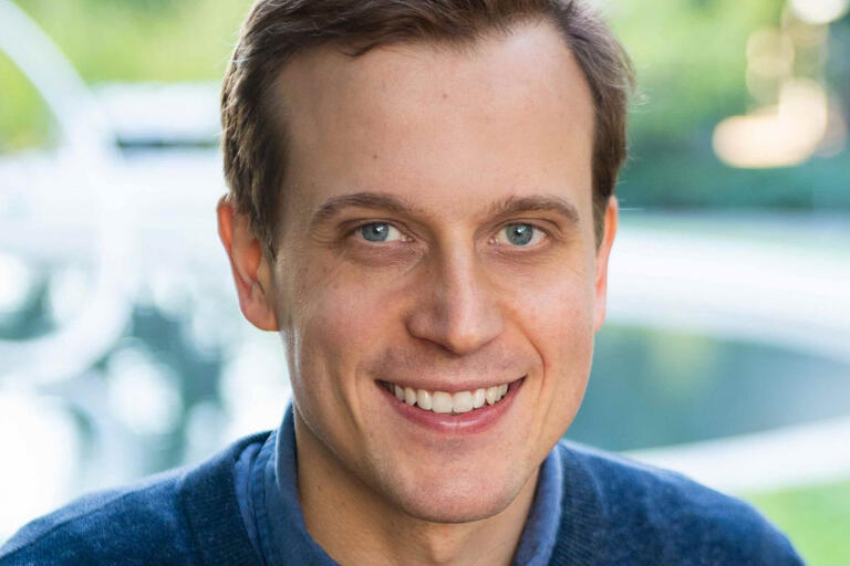 A smiling man with brown hair and a blue sweater