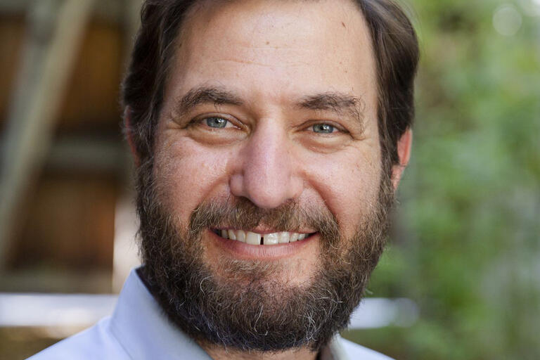 A headshot of a man with brown hair, a beard, and a light blue, button-down shirt