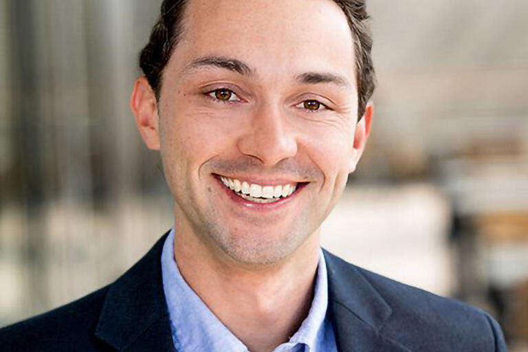 A smiling man wearing a suit jacket with no tie