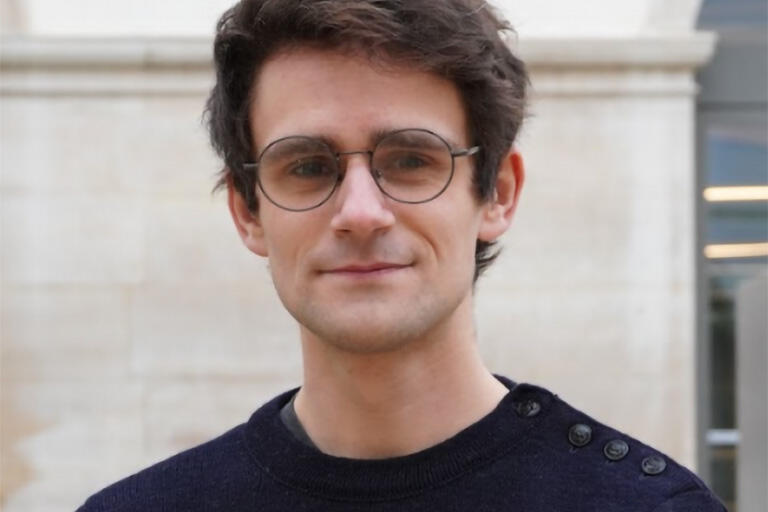 A man with round glasses and a dark blue sweater