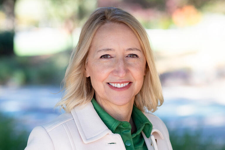 A woman wearing a green shirt and white jacket smiles