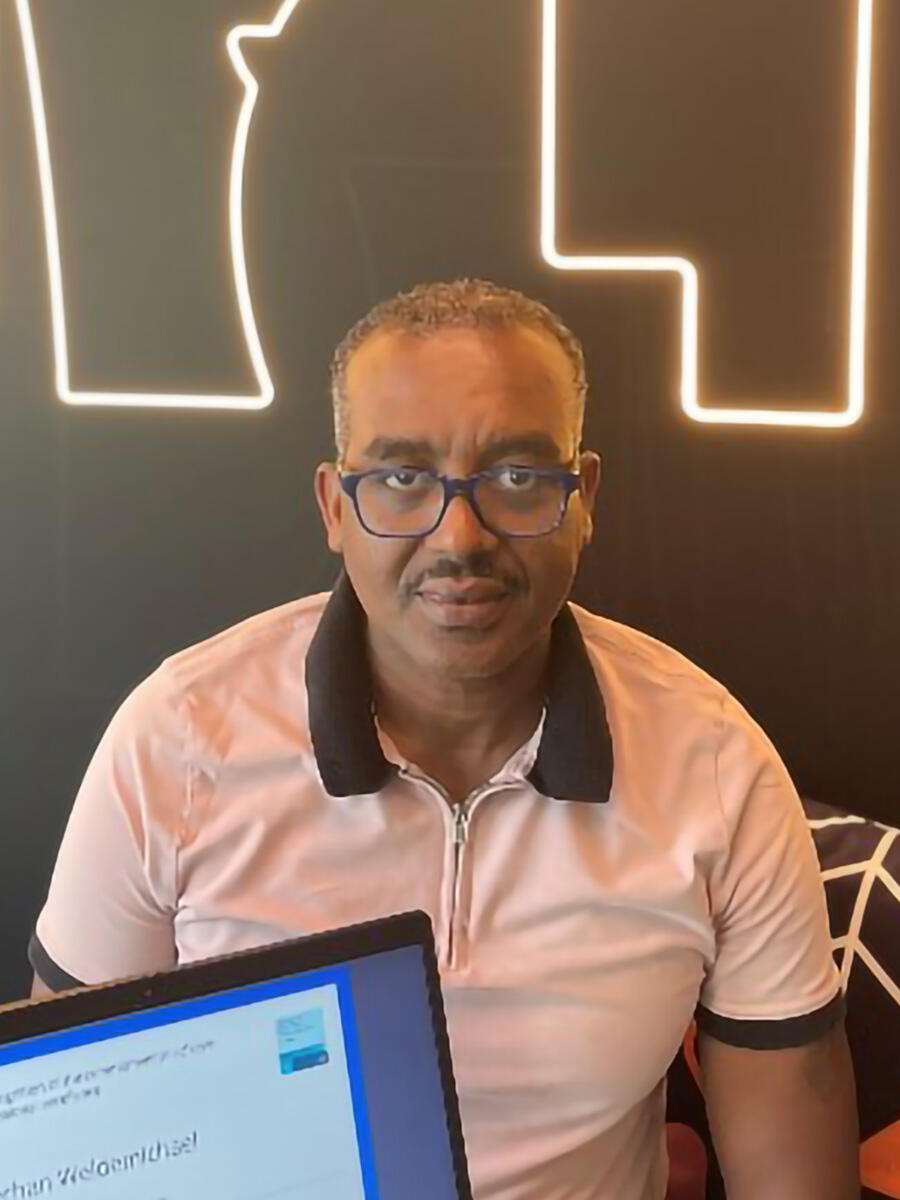 A man with glasses sits on a bench with a computer