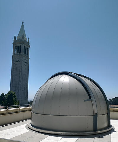 The dome of a telescope on a roof, with the pointed Campanile tower in the background