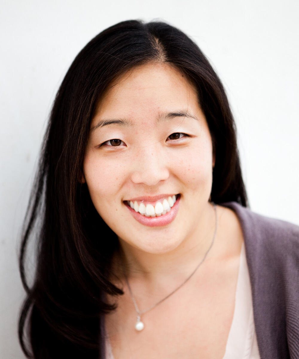 A woman wearing a thin necklace smiles at the camera