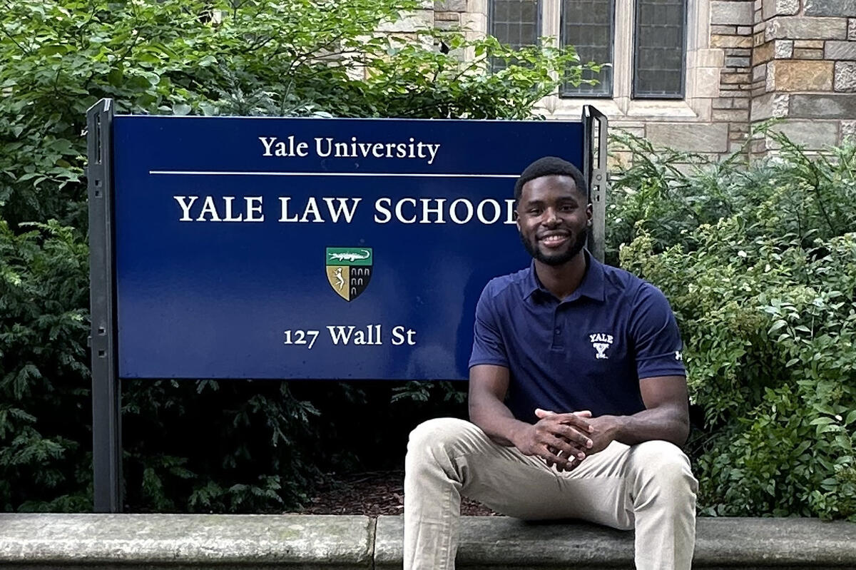 Chaka sits in front of a sign for Yale Law School