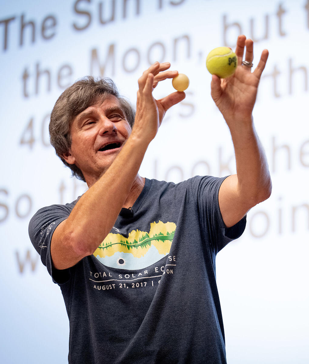 Alex Filippenko holds a ping pong ball and a (farther) tennis ball to demonstrate a solar eclipse.