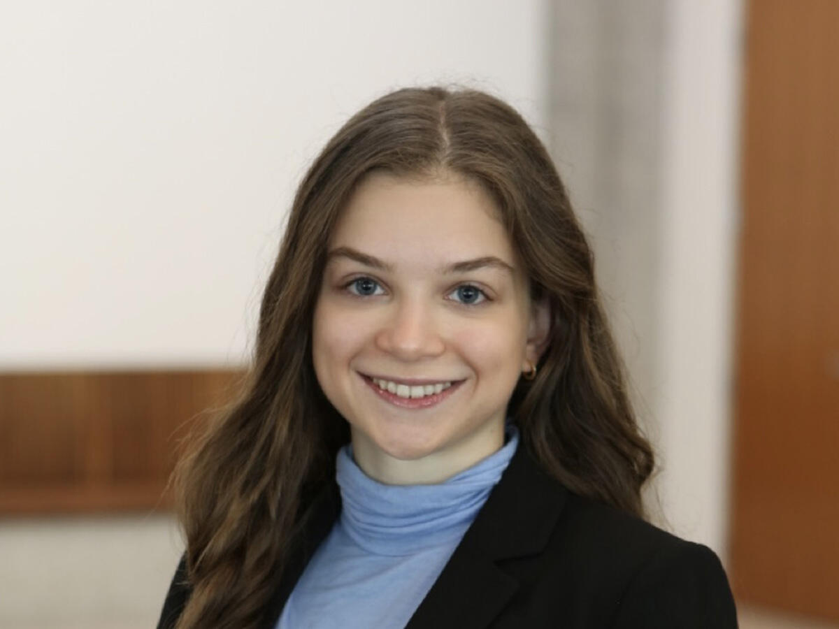 A headshot of Anne Jacobowitz wearing a dark jacket and a light blue shirt with a high collar