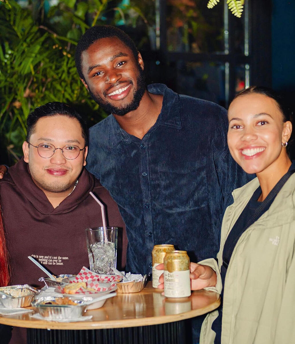 Tellem (center) standing with two friends at a round table with drinks and food in Bogotá