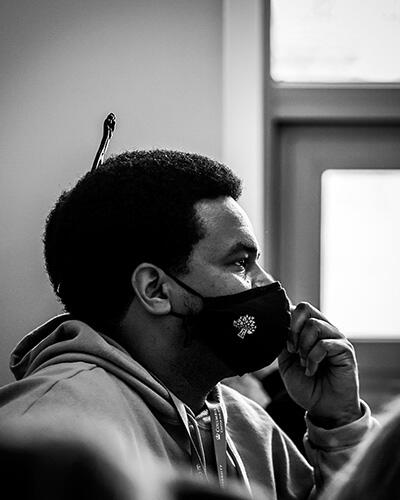 A black-and-white photo of a man wearing a mask and sweatshirt with an afro pick in his hair