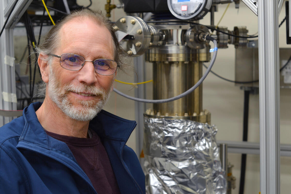 A bearded man with glasses and a blue jacket in front of some metallic equipment