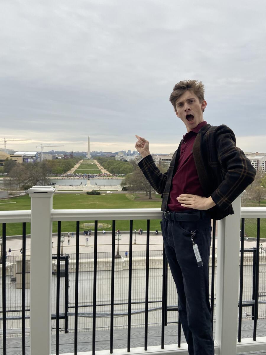 Person standing outside pointing at the Washington Monument with a shocked expression on their face