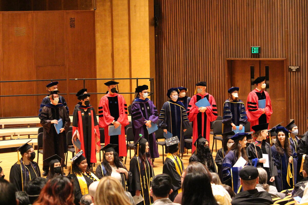 Class of 2022 Linguistic graduates standing below professors at commencement.