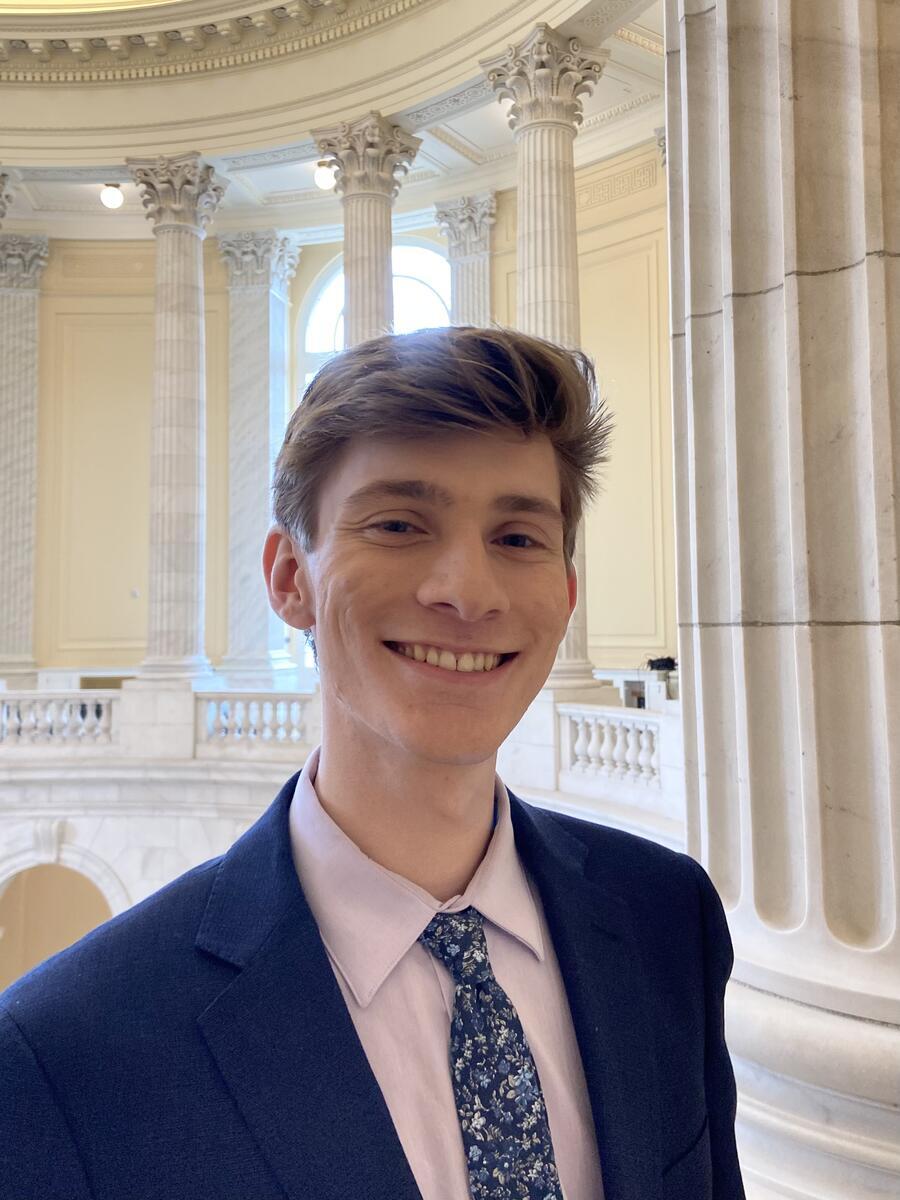 Photo of person wearing a navy suit and tie, standing inside the Capitol building