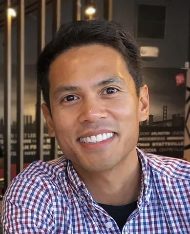 A close-up shot of James Nuñez wearing a checkered shirt and smiling
