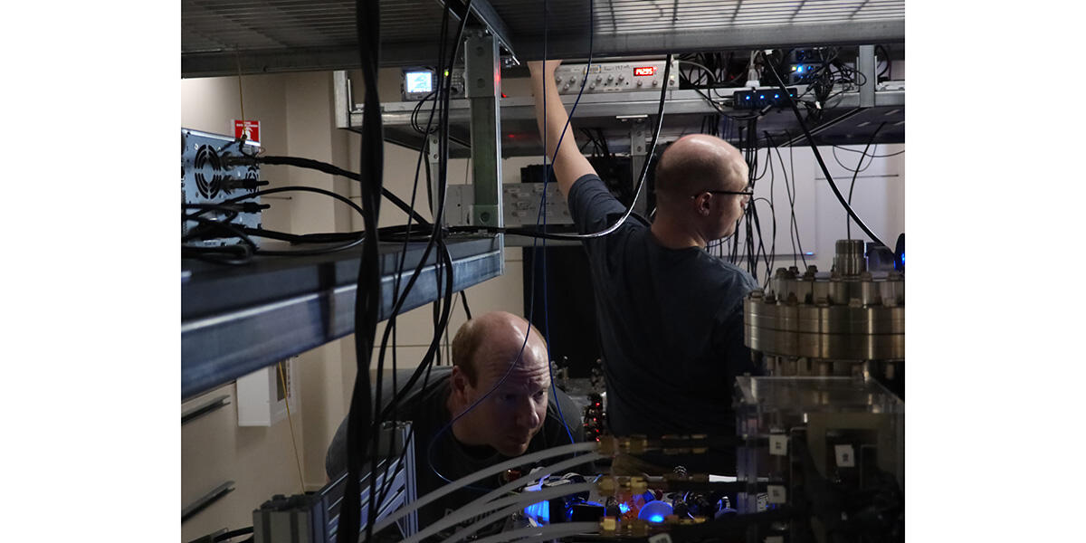 A man tinkers with some settings while another looks intently into a metal chamber