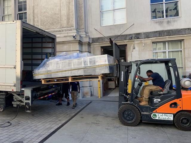 A worker loads a lab table onto a forklift from the back of a truck
