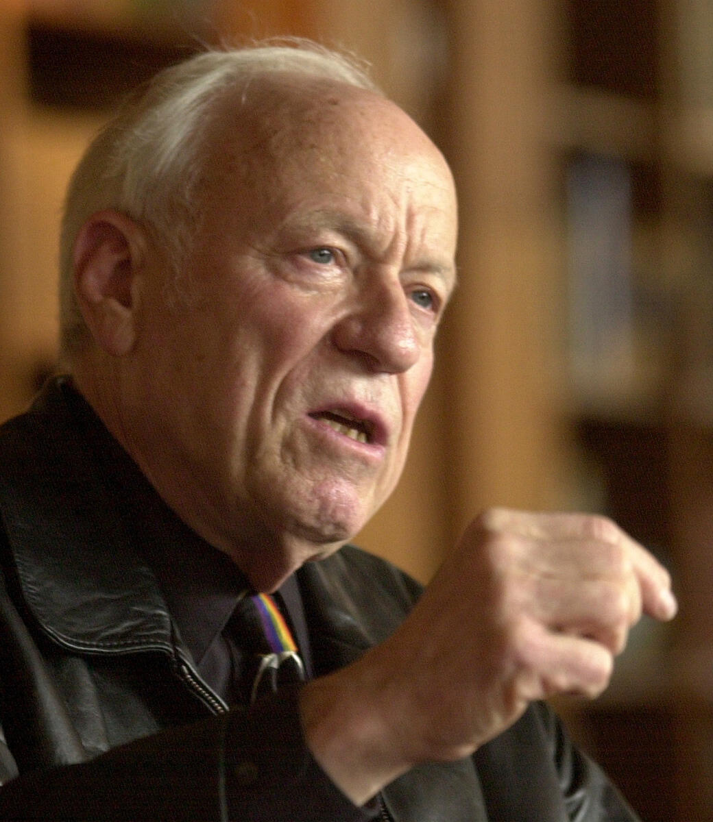 A man in a dark leather jacket gestures with his right hand