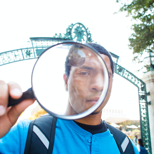 Student with a magnifying glass in front of Sather Gate