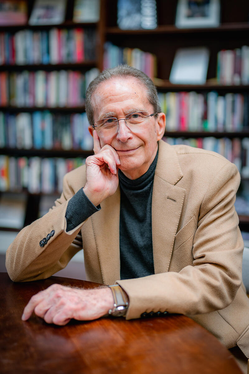 Michael Botchan leans on his hand at a table in front of a crowded bookshelf